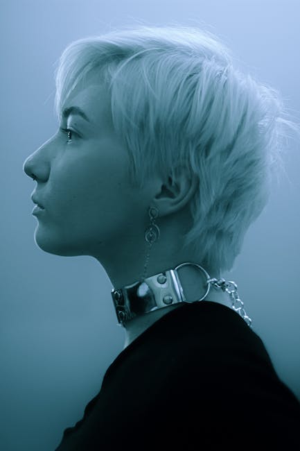 Side view of a young woman with short blonde hair, wearing a silver necklace and earrings.