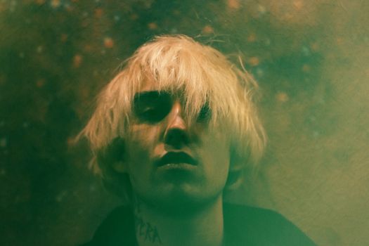 Moody portrait of a blonde man with tattoos, captured in soft focus hues.