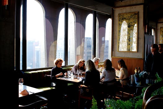 Group of adults enjoying a meal in a stylish city restaurant with large windows.