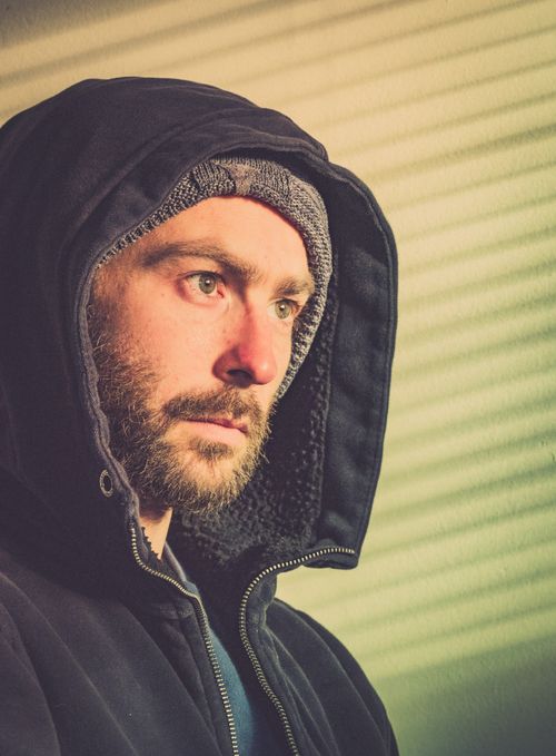 Free Close-up portrait of a bearded man in a black hooded jacket, looking serious. Stock Photo