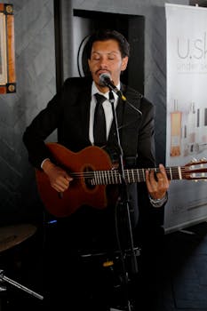A male guitarist in a suit performs indoors, showcasing musical talent.