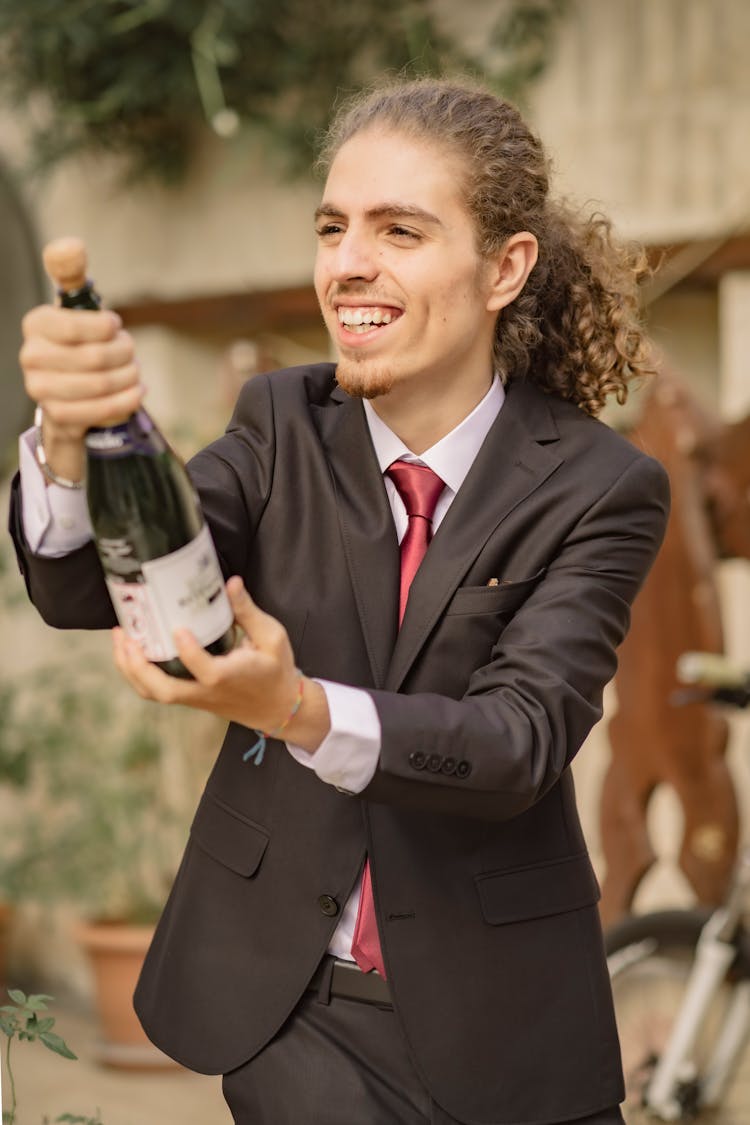 Young Man With Curly Brown Hair Opening Bottle Of Champagne