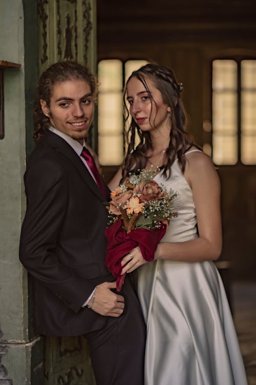 Man in Black Suit and Woman in White Spaghetti Strap Dress with Bouquet of Flowers