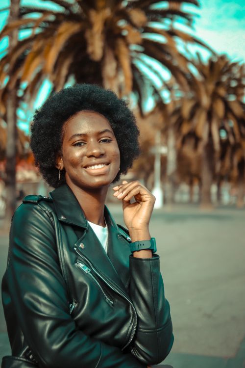 Free A young woman with afro hair wearing a leather jacket smiles in an outdoor setting. Stock Photo