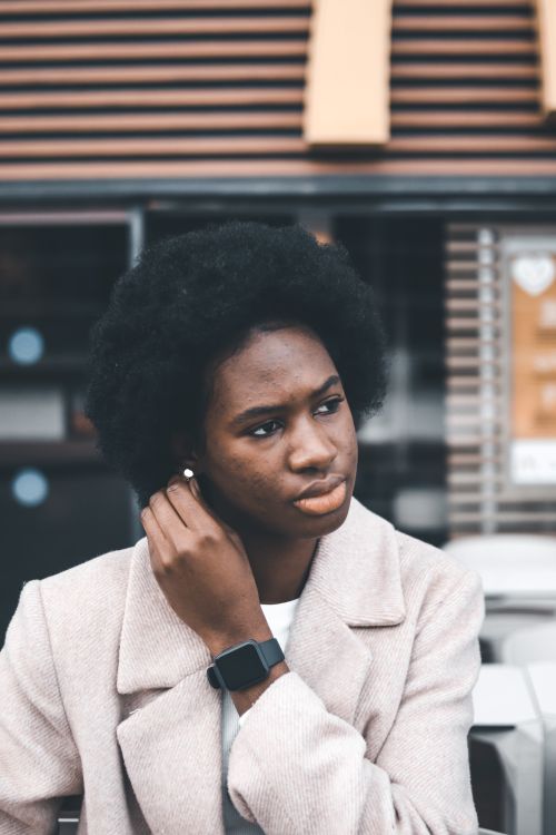 Free Portrait of a thoughtful woman in a coat, sitting outdoors with a smartwatch. Stock Photo