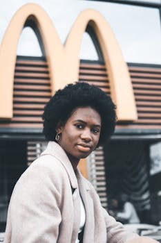 Portrait of a woman with afro hair sitting outside a fast food restaurant, showcasing style and confidence.