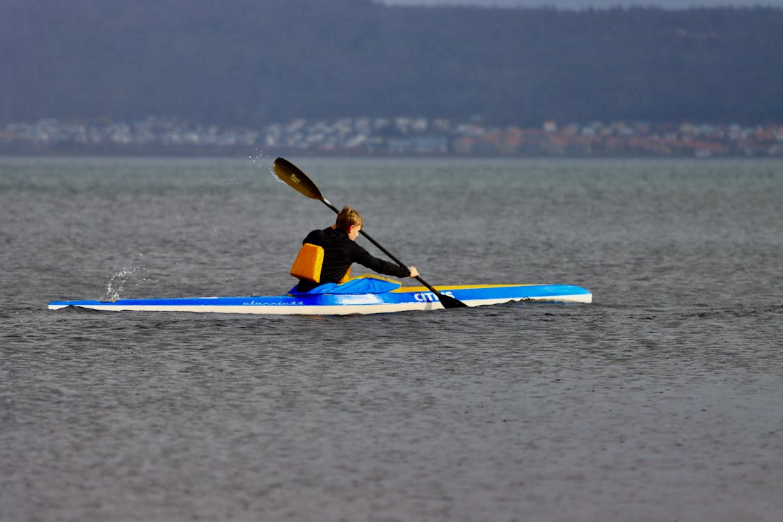 Free Person kayaking across calm waters on Lake Vättern in Jönköping, Sweden, with distant hills. Stock Photo