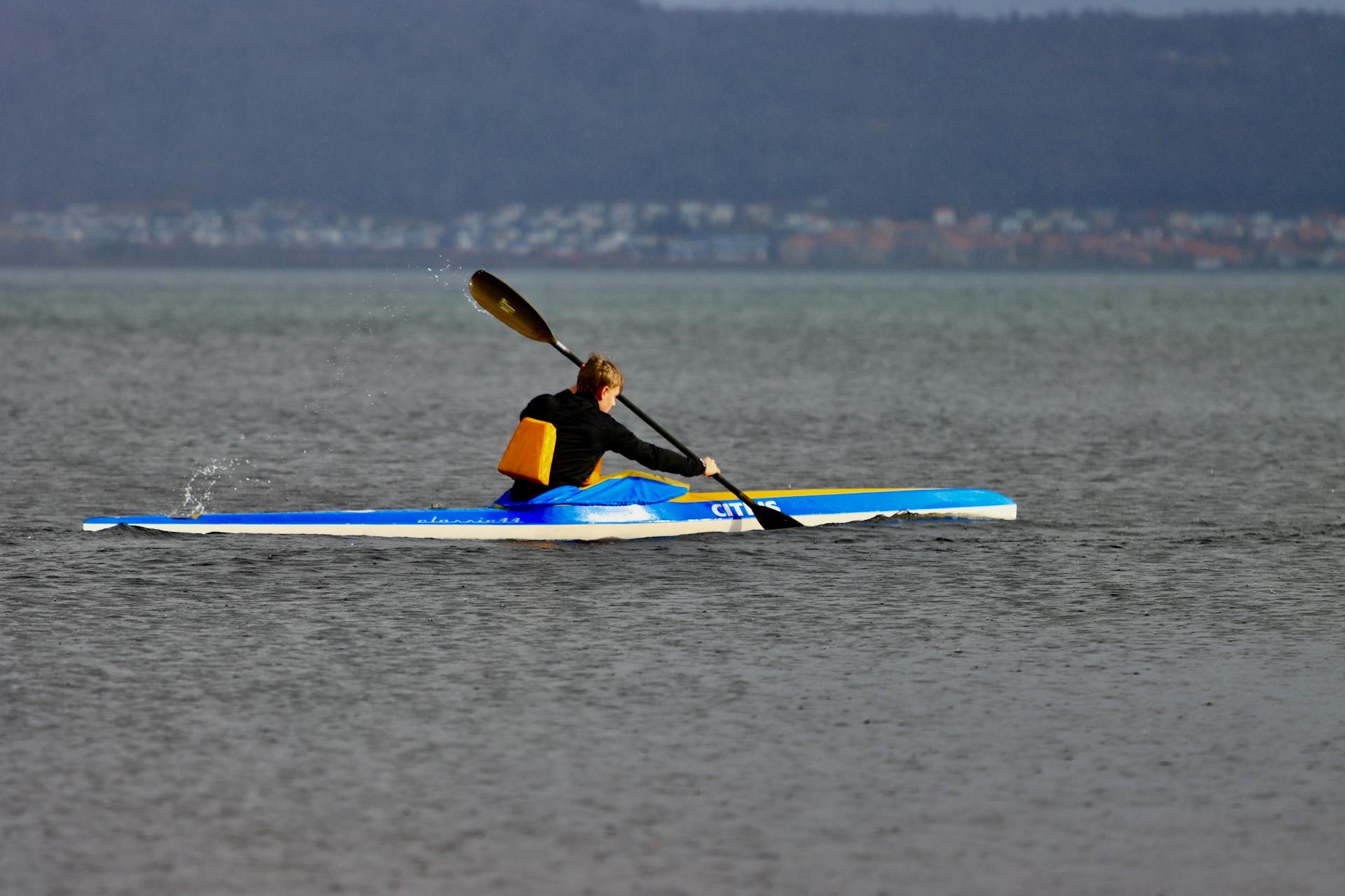 Person kayaking across calm waters on Lake Vättern in Jönköping, Sweden, with distant hills.