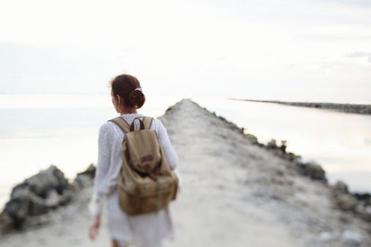 A woman with a backpack walks along a serene coastal path.