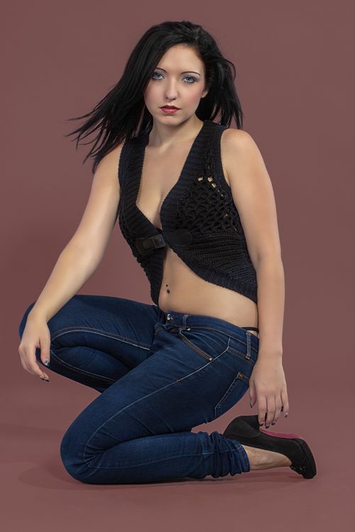 Free Elegant woman posing in a black top and denim jeans against a solid background. Stock Photo