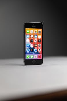 Close-up of a black smartphone displaying various app icons on a white surface.