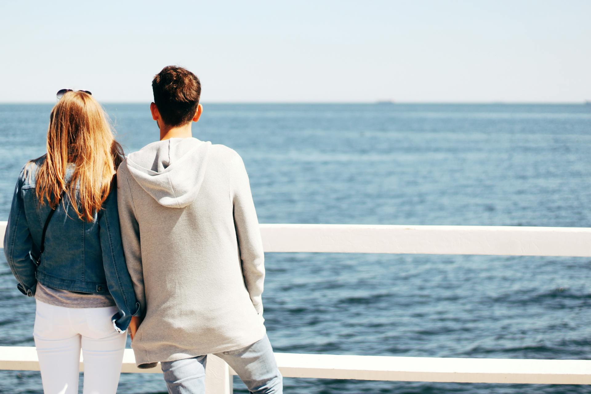 A couple leans on a railing, enjoying a serene ocean view on a sunny day.