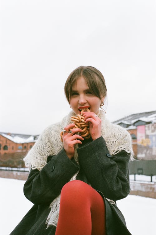 Woman in Black Coat Biting a Bread Ring 