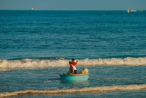 Free Two fishermen in a small boat on a peaceful coastline in Vietnam, enjoying a tranquil fishing day. Stock Photo