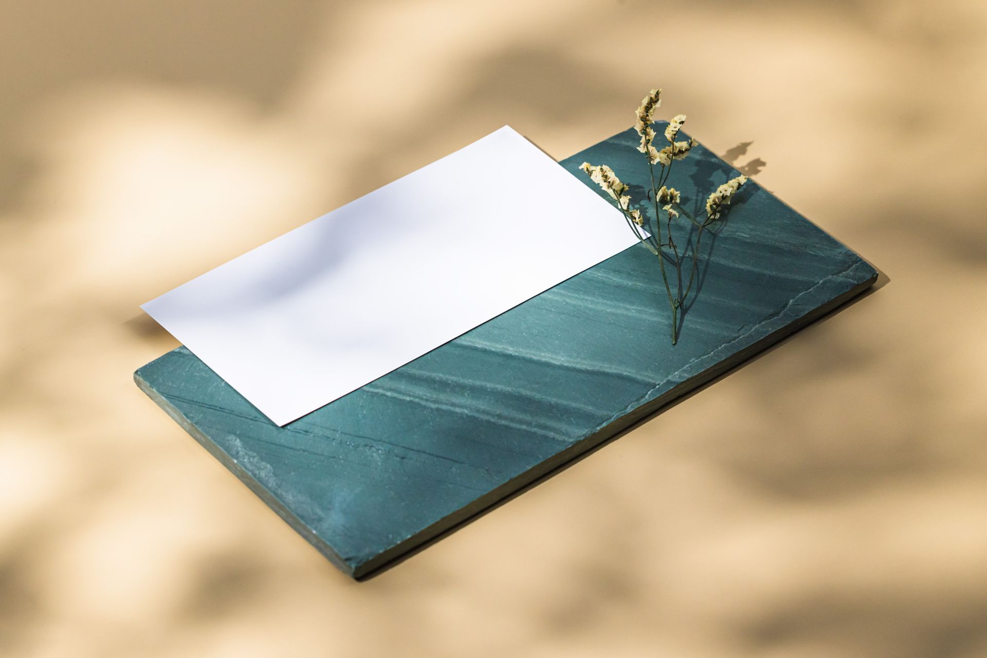 Minimalist stationery on green slate with delicate flowers, artistic lighting.