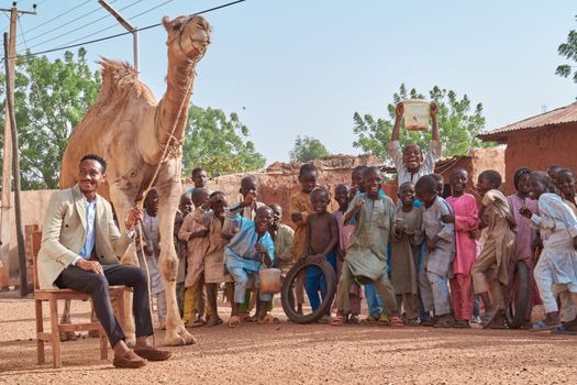 A cheerful gathering of people with a camel in an outdoor African village setting, full of life and happiness.
