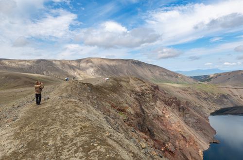 Free Expansive view of Kamchatka's rugged landscape with hikers on the rocky terrain under a blue sky. Stock Photo