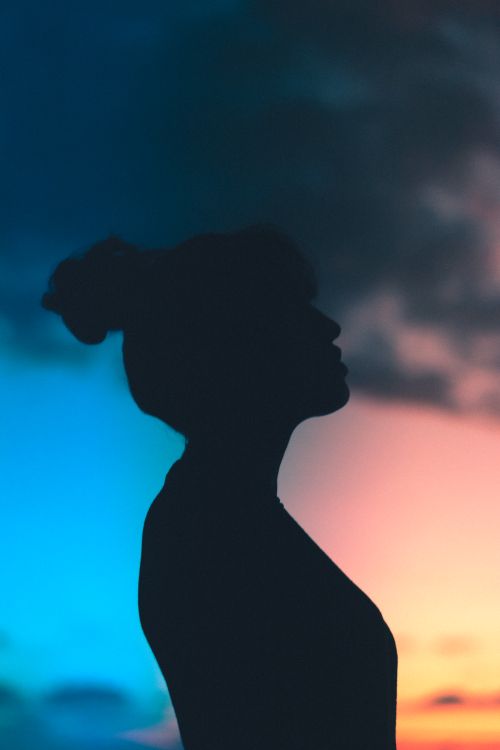 Free Artistic silhouette of a woman against a vibrant twilight sky, blending blue and orange hues. Stock Photo