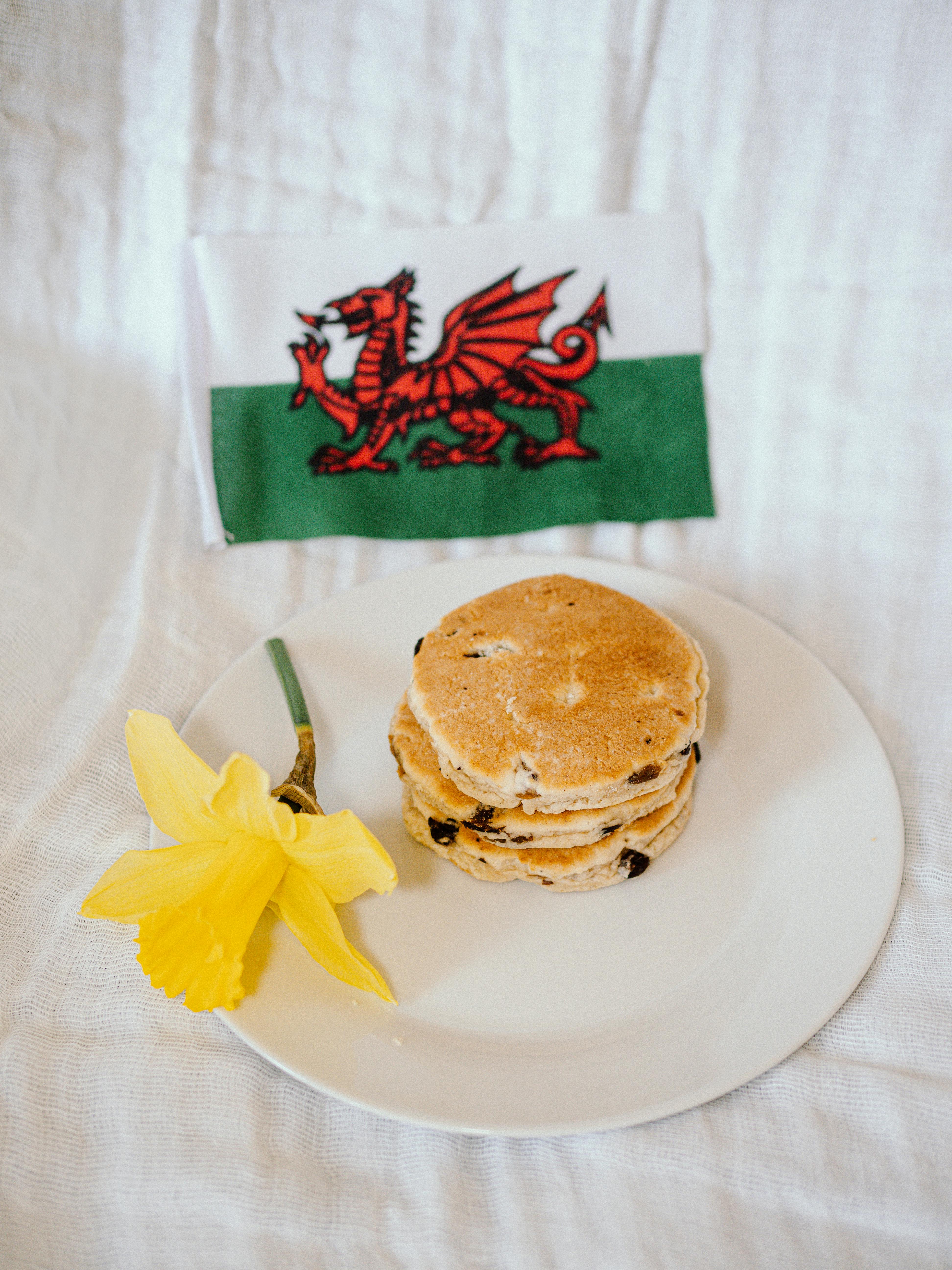 Stack of traditional Welsh cakes with a daffodil and Welsh flag on cloth.