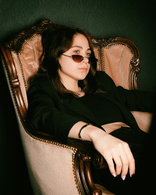 Woman in Black Long Sleeve Shirt Wearing Black Sunglasses Sitting on Brown Armchair