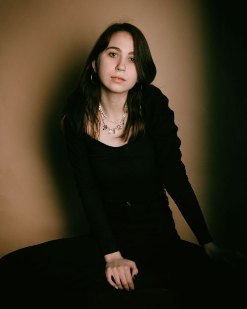 Free Portrait of a young woman in black attire with elegant jewelry sitting against a neutral backdrop. Stock Photo