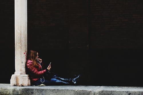 無料 スマートフォンを持っている柱に座っている女性の写真 写真素材
