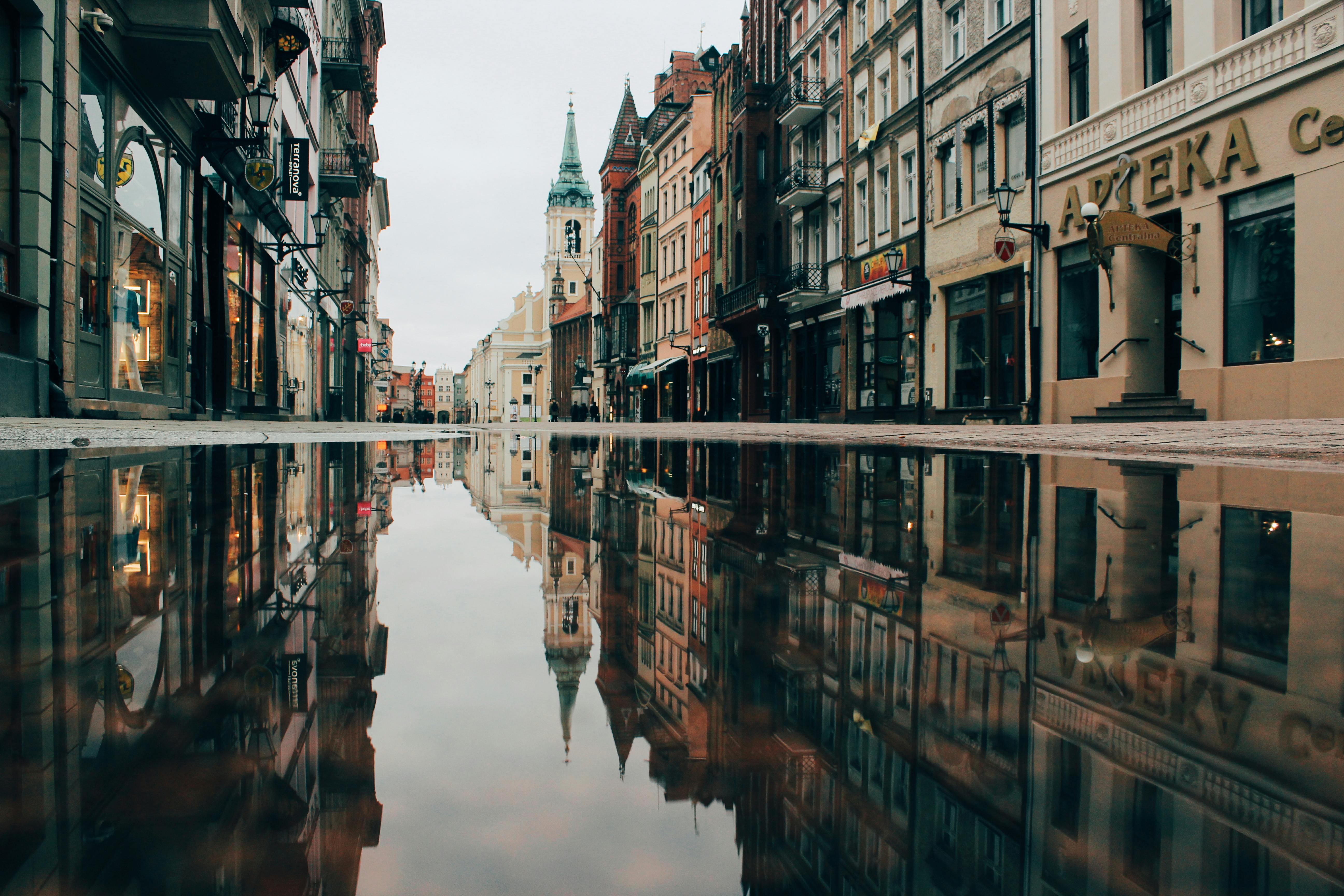 Colorful European buildings and church tower reflected in a puddle on a quiet cobblestone street after rain.