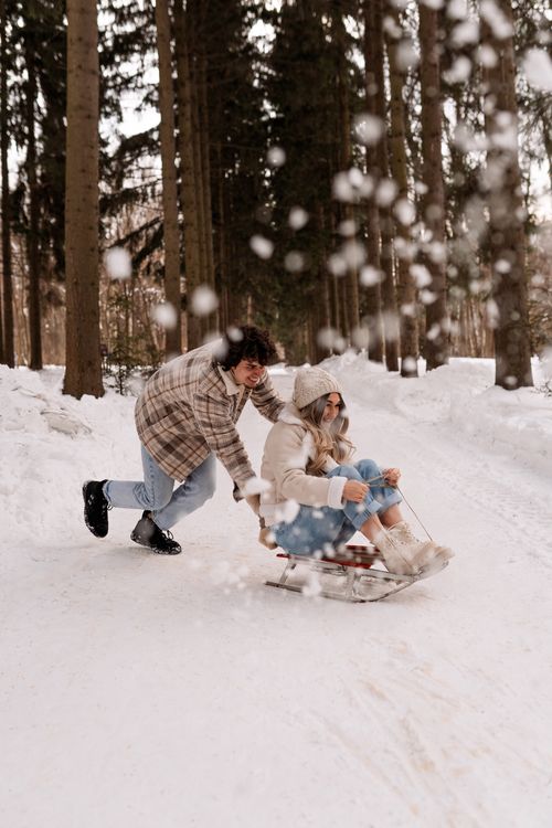 Free A couple enjoys a playful sled ride through a snowy forest, capturing winter fun. Stock Photo