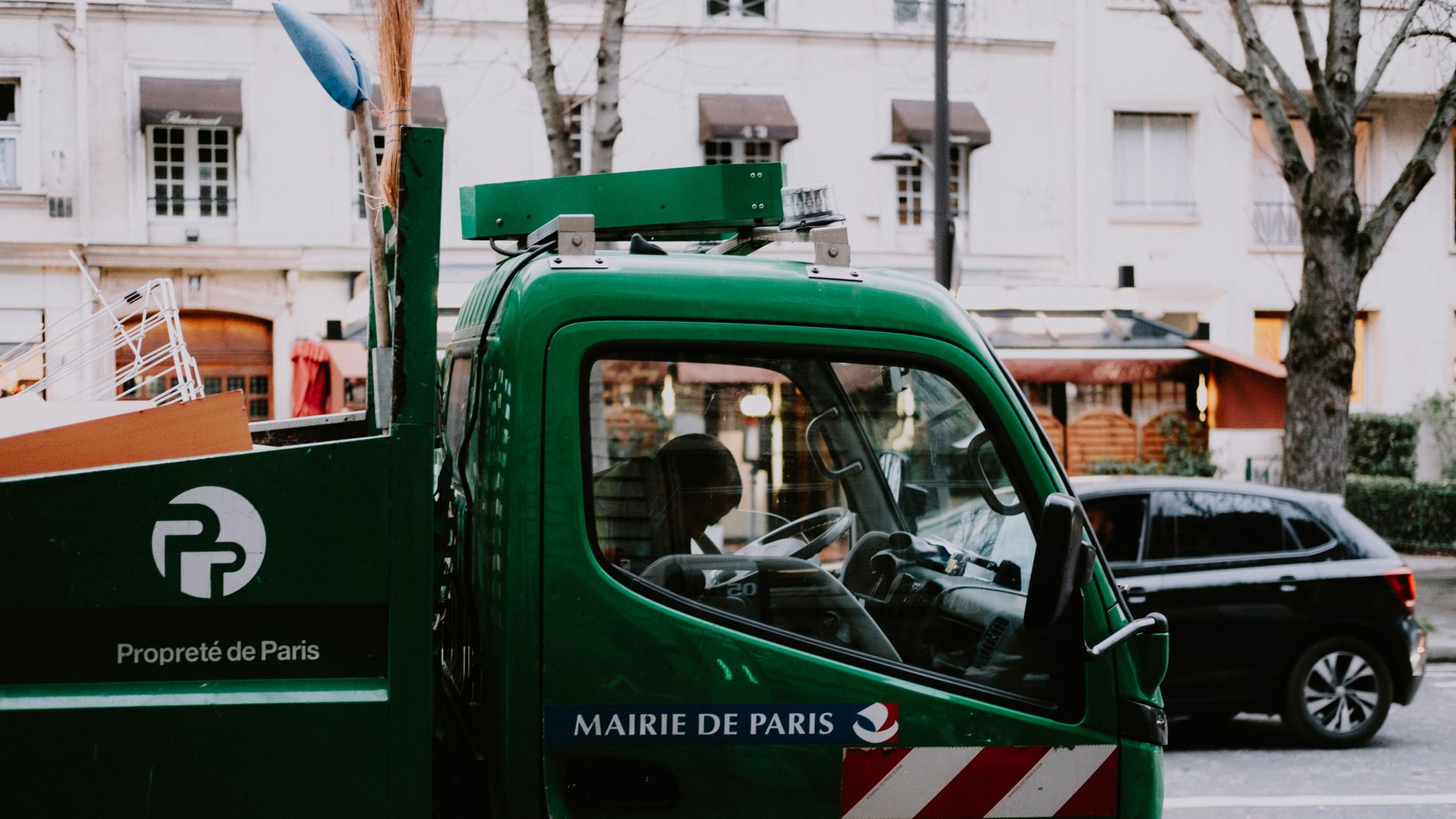 A green city garbage truck, marked 'Propreté de Paris,' on a Parisian street with urban backdrop.