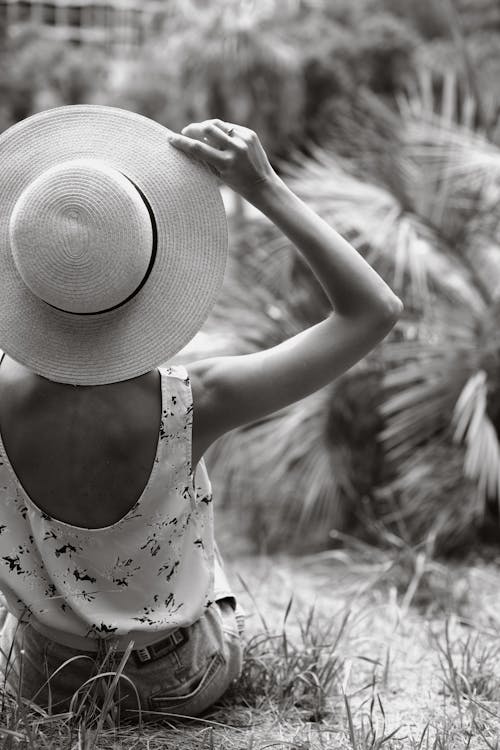 Woman in White Sleeveless Shirt Wearing Hat Sitting on Grass