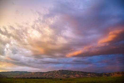 Vibrant sunset sky over a serene countryside landscape with rolling hills.