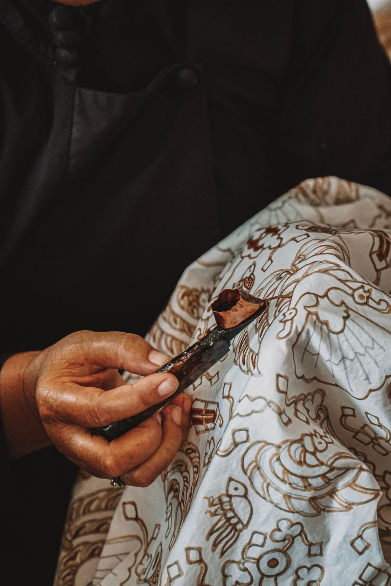 Tangan mengerjakan batik tulis dengan canting di atas kain