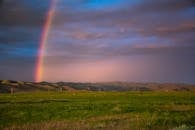 日落时分，郁郁葱葱的田野和连绵起伏的山丘上，点缀着五彩缤纷的彩虹