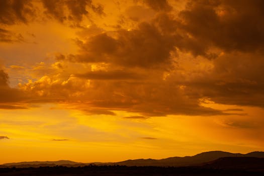 Dramatic golden sunset with clouds over a mountainous landscape, capturing the essence of nature and serenity.