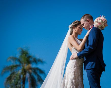 Bride and groom share a tender moment outdoors under a blue sky in Paraguay.