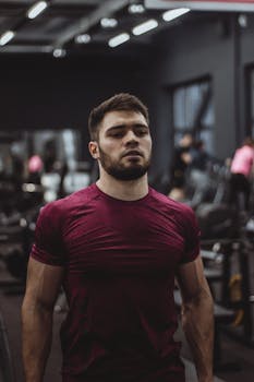 Athletic young man with a beard working out in the gym, wearing a red shirt.