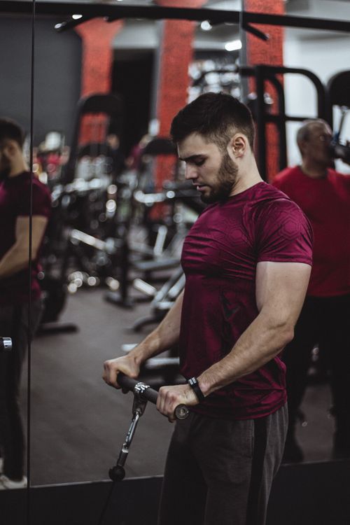 Free Muscular man with facial hair working out in gym setting, side view captured. Stock Photo