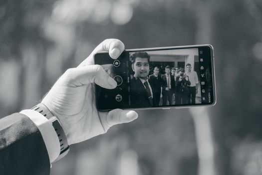 A black and white photo of a group selfie taken with a smartphone outdoors.
