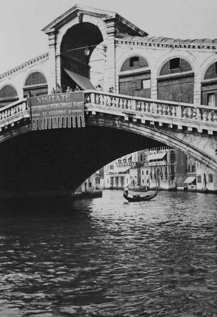 Black and white image of Rialto Bridge in Venice with gondola on the Grand Canal.