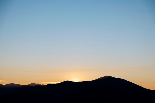 A serene sunrise over the rolling hills of the French Basque Country, capturing warm tones and silhouetted landscape.