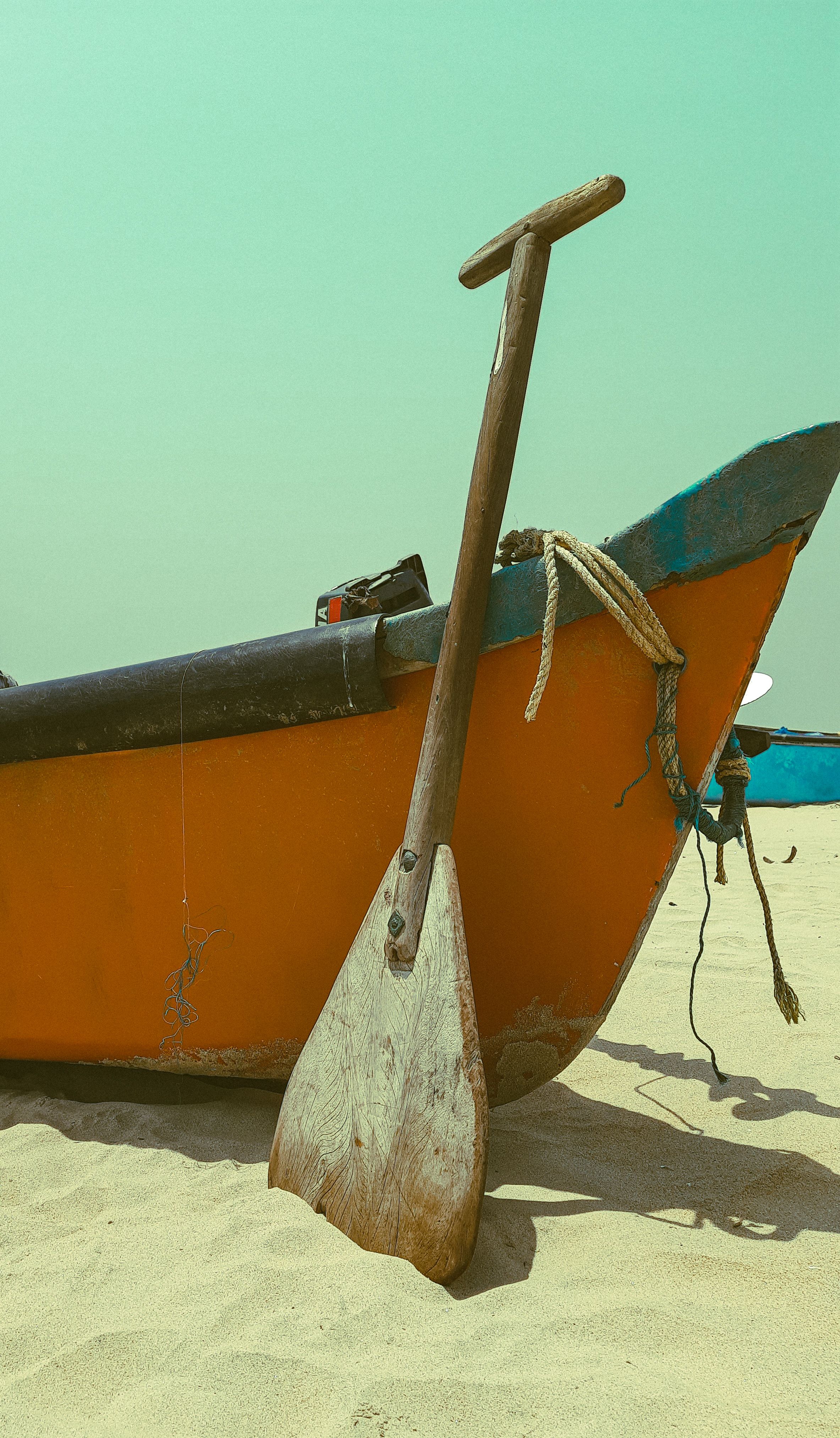 Close-up of an orange fishing boat and wooden paddle on a sandy beach in Kasaragod, Kerala.