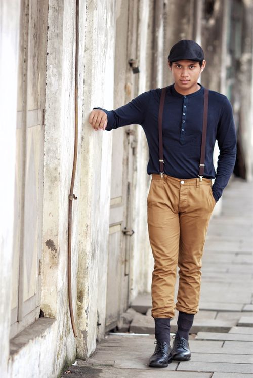 Free A fashionable man wearing suspenders poses against a textured wall outdoors. Stock Photo