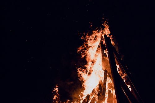 Free A dramatic close-up shot of a roaring bonfire with tall flames against a dark night sky. Stock Photo
