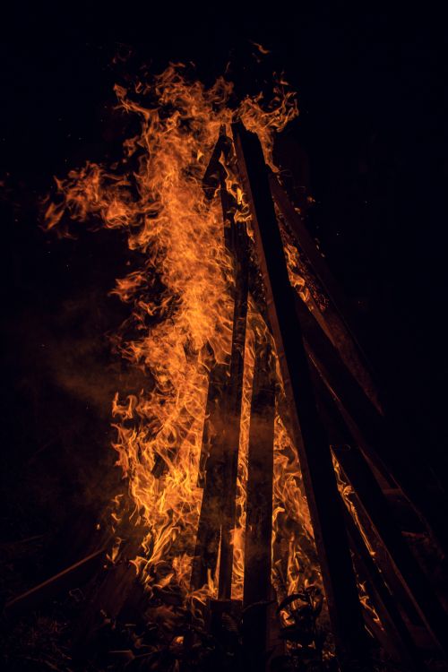 Free Vertical shot of a blazing bonfire with tall wooden planks engulfed in flames during nighttime. Stock Photo