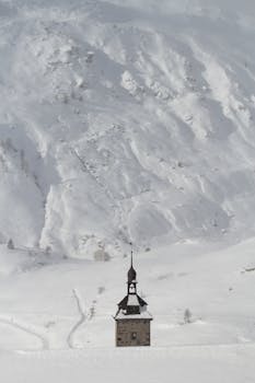 Serene winter scene featuring a snow-covered church with a prominent steeple against a mountainous backdrop.