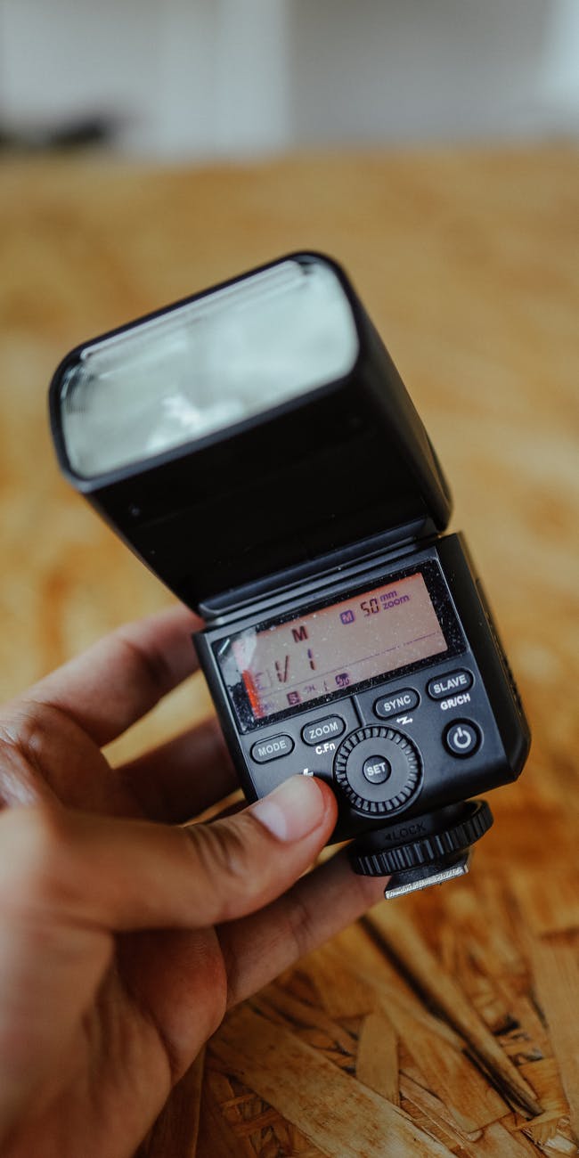 Detailed view of a hand holding a digital camera flash against a wooden backdrop.