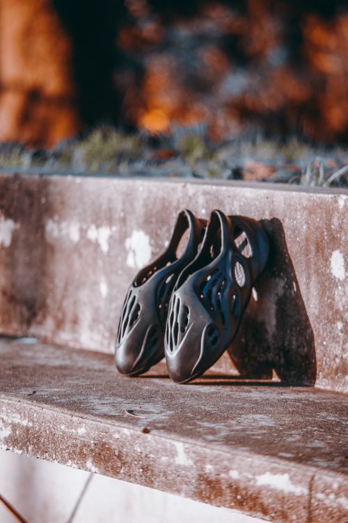 Free Pair of fashionable foam runner shoes resting on a concrete bench, highlighting modern footwear design. Stock Photo