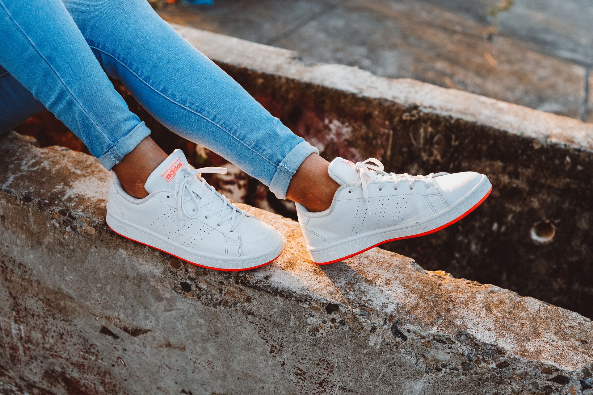 Person wearing white sneakers and denim jeans on a concrete surface outdoors.