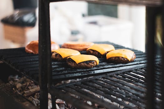 Close-up of cheeseburgers cooking on a charcoal barbecue grill, perfect for outdoor summer gatherings.