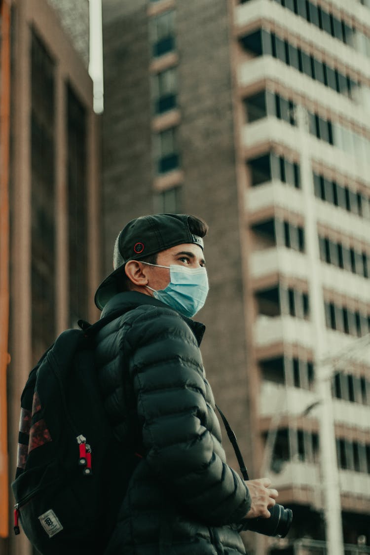 Young Man Standing In Winter Jacket Wearing Face Mask Holding Camera